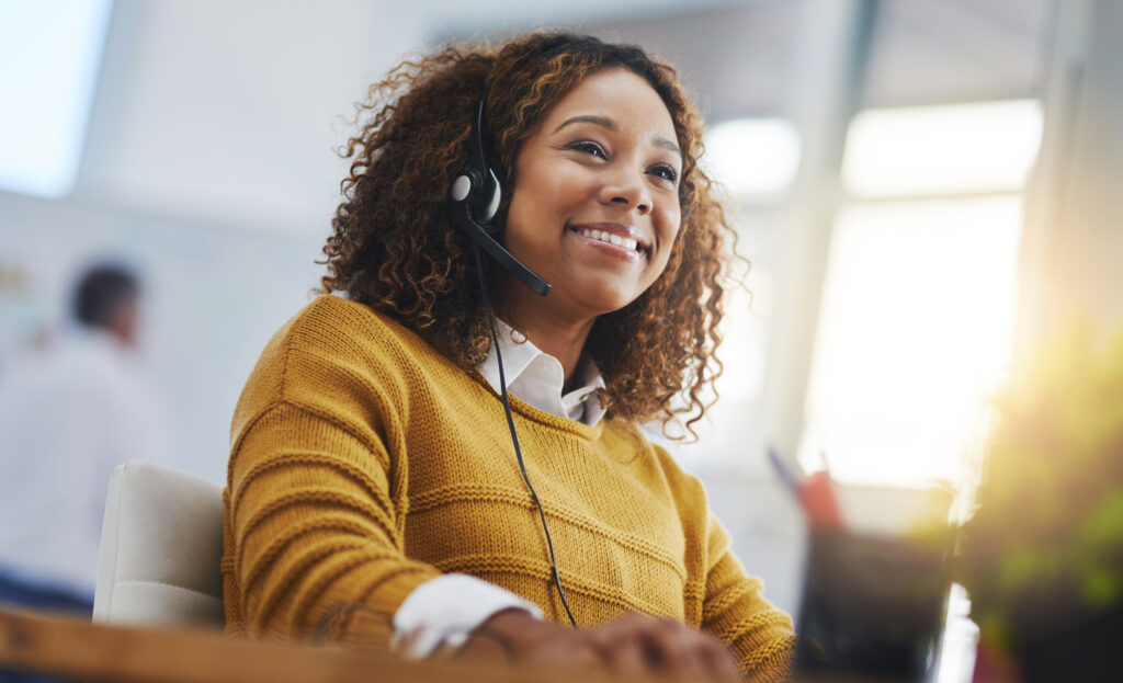 vrouw die werkt als callcenter-agent, glimlachend terwijl ze een VoIP-telefoon gebruikt voor klantenservice en technische ondersteuning in een kantooromgeving.