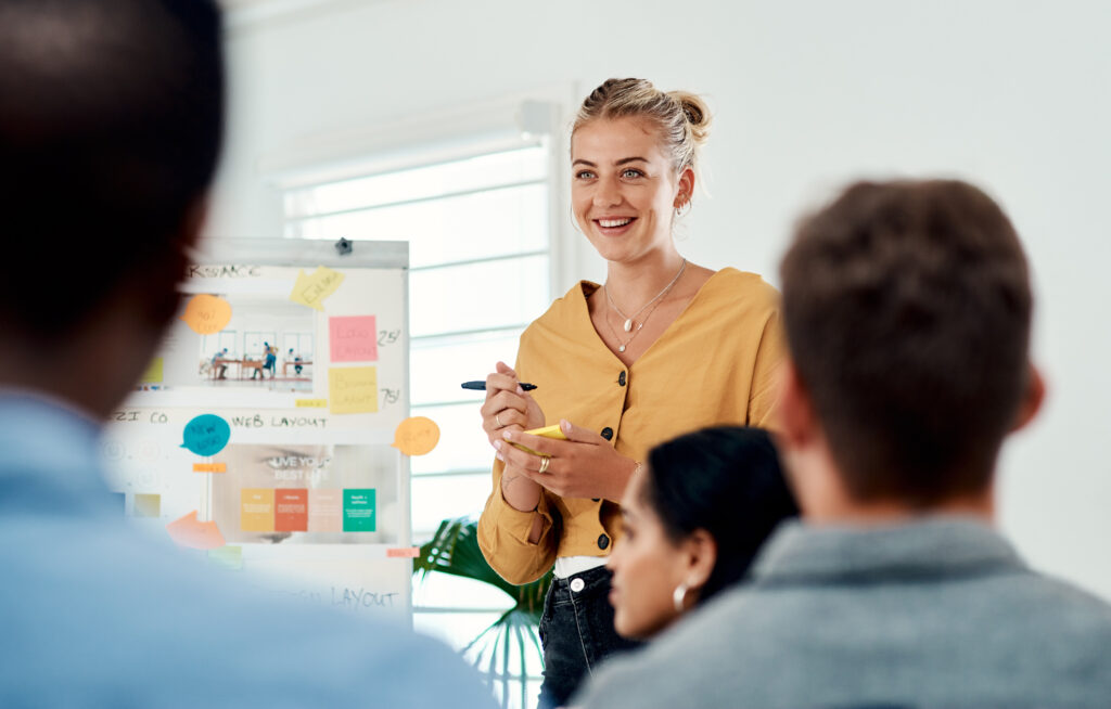 Zakenvrouw geeft een presentatie tijdens een vergadering, terwijl collega's aandachtig luisteren en samenwerken aan creatieve ideeën.